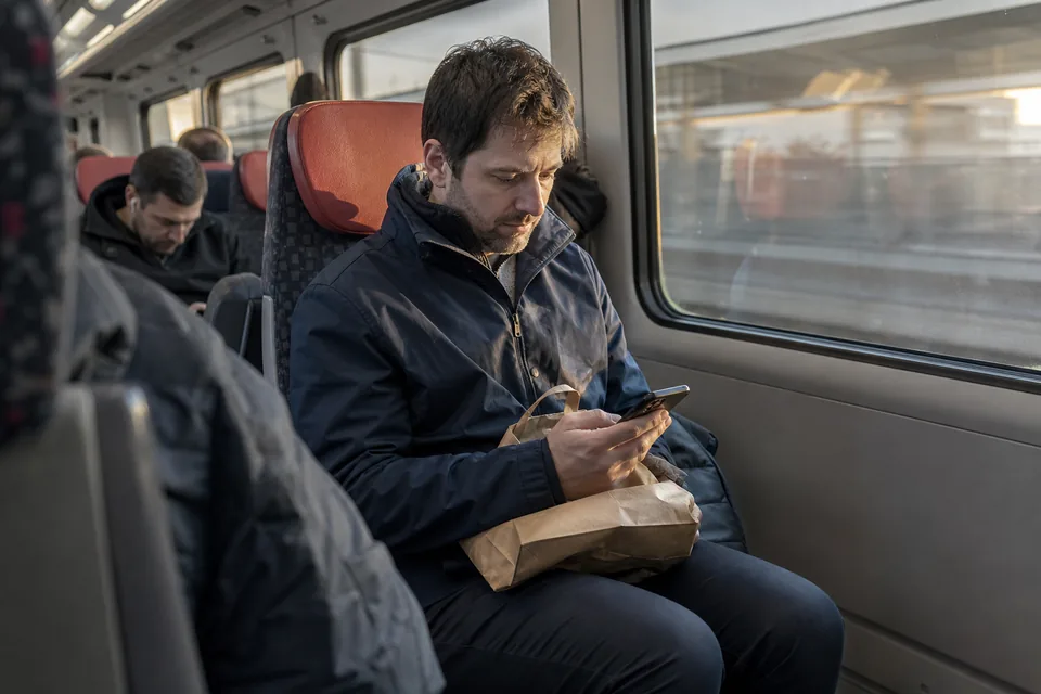 Man on a commuter train glancing at a text message notification on his phone, shopping bag on his lap