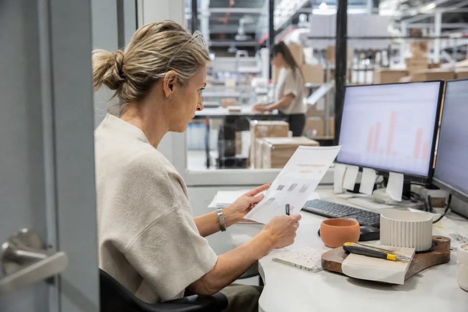 Ecommerce director comparing a printed revenue report with figures on her second monitor