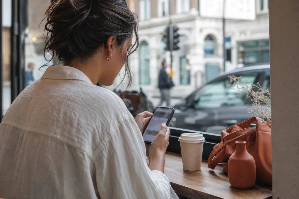 Shopper hesitating at the checkout step on a smartphone in a cafe